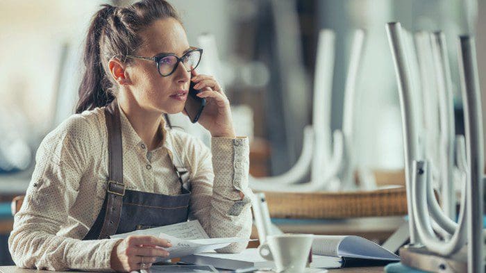 A woman who operates a local cafe reviewing invoices and bookkeeping while on a phone call